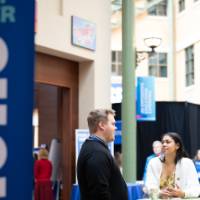 2 people talking at a table with the Reach Higher Showcase banner in view